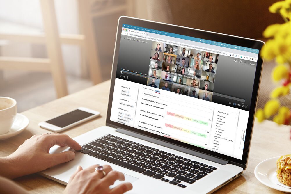 A Content Parent uses a laptop on a wooden table, attending a video conference with many participants. The screen also displays a document or spreadsheet below the video call window.