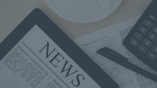 A tablet displaying a news article, a printed chart, a pen, a calculator, and part of a coffee cup on a desk—tools shaping the future of sales team strategies and employee development.